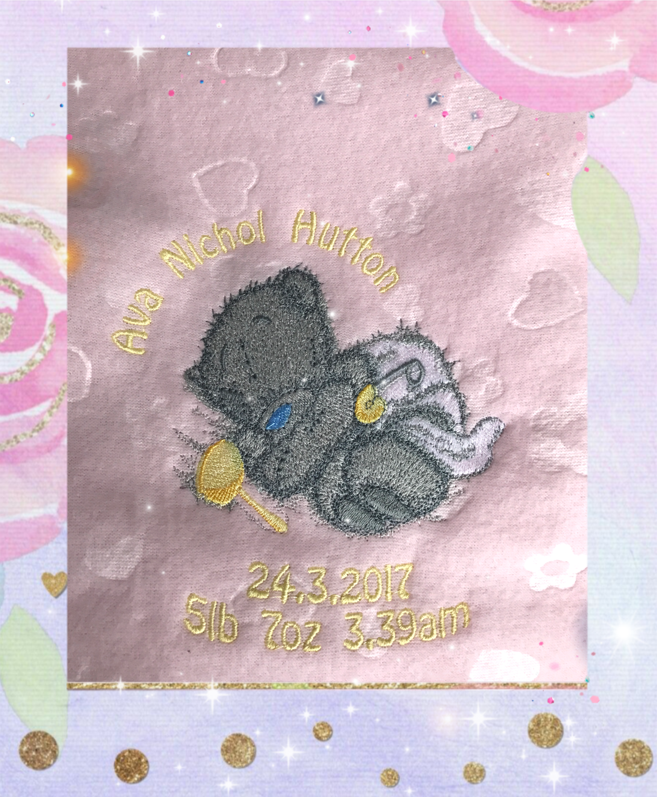 Grey Tatty Teddy asleep in a nappy, embroidered on a light pink fleece blanket with a yellow rattle.